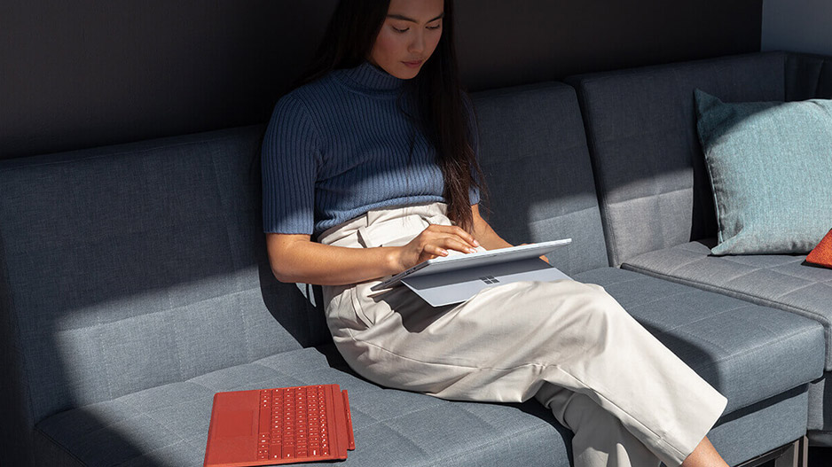 一位女性坐在沙发上工作，膝盖上放着 Surface Pro 7