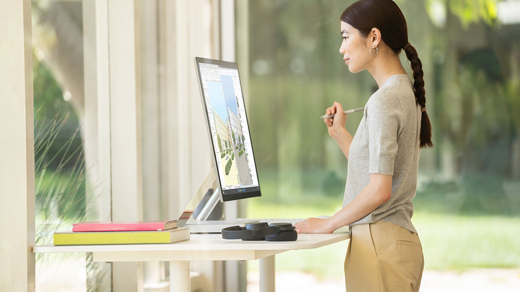 一人站在桌子前使用  Surface Studio 2+ 商用版。