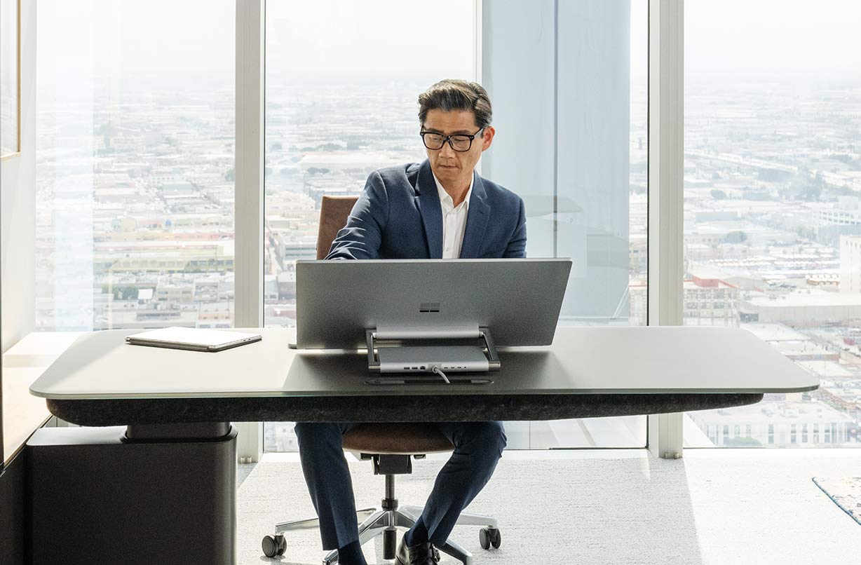 一个人坐在桌前，在 Surface Studio 2+ 商用版上工作。