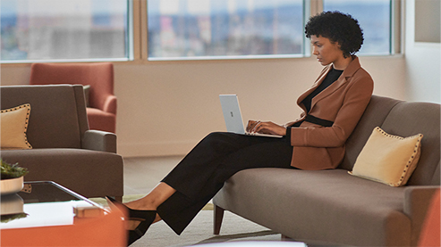 办公室环境中，一个人坐在沙发上操作 Surface 设备。